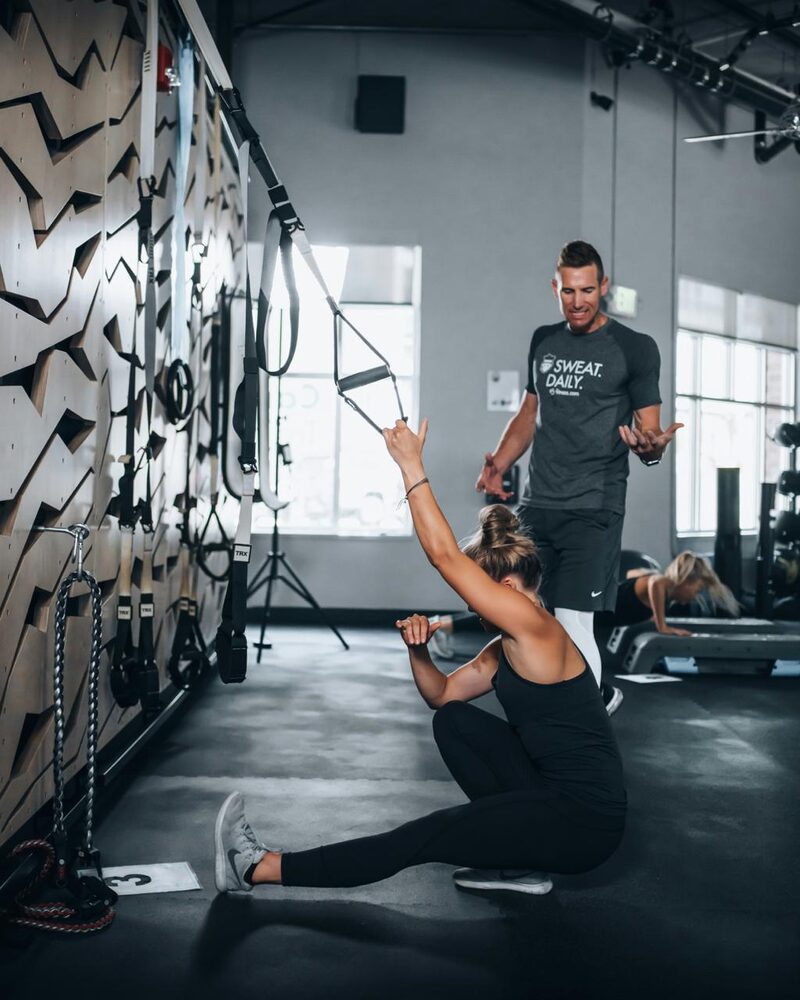 Coach accompagnant une femme lors d'un entraînement TRX
